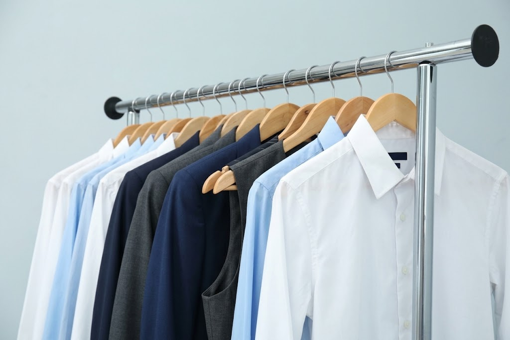 Uniformes administrativos en perchas: camisas blancas y celestes, chaquetas y chalecos en azul y gris